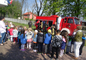 Dzieci stoją na dworze wokół wozu strażackiego.